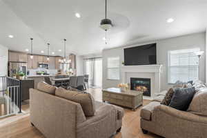 Living room with vaulted ceiling, ceiling fan with notable chandelier, plenty of natural light, and light LVP flooring