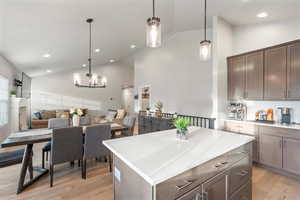 Kitchen featuring tasteful backsplash, lofted ceiling, a center island and decorative light fixtures