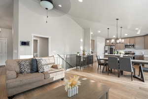 Living room featuring light wood-type flooring, ceiling fan with notable chandelier, and high vaulted ceiling