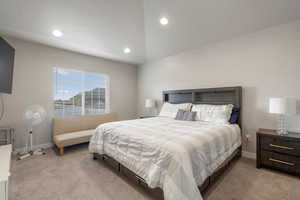 Master bedroom with light carpet and vaulted ceiling