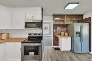 Kitchen featuring wood counters, white cabinets, light hardwood / wood-style flooring, backsplash, and appliances with stainless steel finishes