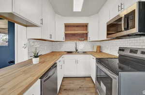 Kitchen with stainless steel appliances, white cabinets, butcher block countertops, and light wood-type flooring