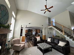 Living room featuring high vaulted ceiling, ceiling fan, a fireplace, and dark wood-type flooring