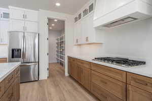 Kitchen featuring white cabinets, custom exhaust hood, light hardwood / wood-style flooring, appliances with stainless steel finishes, and light stone countertops