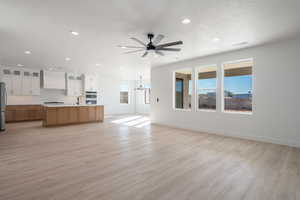 Unfurnished living room featuring ceiling fan with notable chandelier, sink, and light hardwood / wood-style flooring