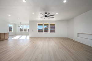 Unfurnished living room featuring ceiling fan with notable chandelier and light hardwood / wood-style flooring