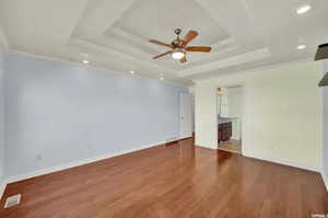 Empty room with a raised ceiling, ornamental molding, ceiling fan, and wood-type flooring