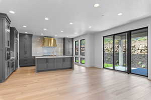 Kitchen with gray cabinets, light hardwood / wood-style floors, oven, and a center island with sink