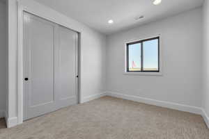 Unfurnished bedroom with a textured ceiling, light colored carpet, and a closet