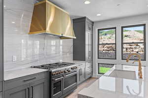 Kitchen with light stone counters, gray cabinets, wall chimney range hood, and double oven range