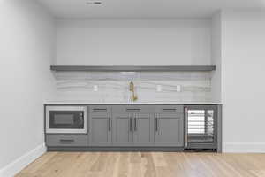 Bar with beverage cooler, light wood-type flooring, sink, and black microwave