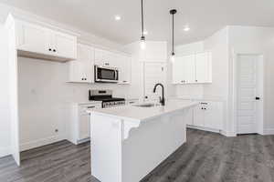 Kitchen featuring appliances with stainless steel finishes, sink, white cabinetry, hanging light fixtures, and an island with sink