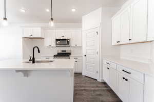 Kitchen with appliances with stainless steel finishes, sink, pendant lighting, and white cabinetry