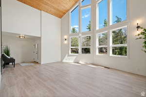 Unfurnished living room featuring a notable chandelier, wood ceiling, light hardwood / wood-style flooring, and high vaulted ceiling