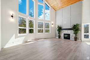 Unfurnished living room featuring light wood-type flooring, wood ceiling, a fireplace, and high vaulted ceiling