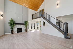 Unfurnished living room featuring light hardwood / wood-style floors, wood ceiling, high vaulted ceiling, a fireplace, and french doors