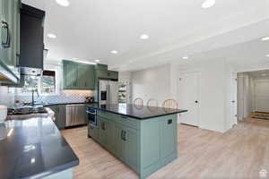 Kitchen with sink, a kitchen island, green cabinetry, light hardwood / wood-style flooring, and stainless steel appliances