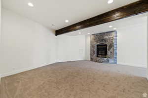 Unfurnished living room featuring a stone fireplace, beam ceiling, and carpet