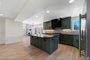 Kitchen with pendant lighting, light wood-type flooring, a center island, custom range hood, and high end range