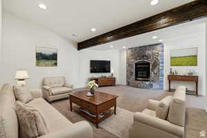 Carpeted living room with a stone fireplace and beam ceiling