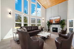 Living room with light wood-type flooring, wood ceiling, a high end fireplace, and high vaulted ceiling