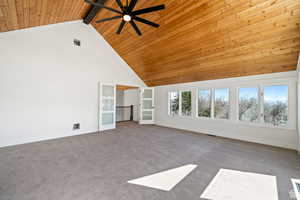 Unfurnished living room featuring ceiling fan, carpet flooring, beam ceiling, high vaulted ceiling, and wooden ceiling