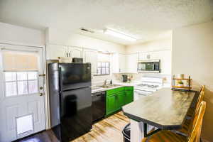 Kitchen featuring green cabinets, a wealth of natural light, black appliances, and white cabinetry