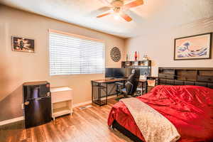 Bedroom featuring a textured ceiling, hardwood / wood-style floors, black fridge, and ceiling fan