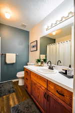 Bathroom with a textured ceiling, hardwood / wood-style flooring, vanity, and toilet