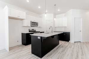 Kitchen featuring hanging light fixtures, stainless steel appliances, an island with sink, white cabinets, and sink