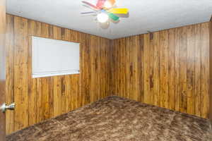 Carpeted empty room featuring ceiling fan and wooden walls