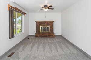 Unfurnished living room with a brick fireplace, carpet, and ceiling fan