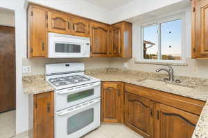 Kitchen featuring light stone countertops, white appliances, light tile patterned flooring, and sink