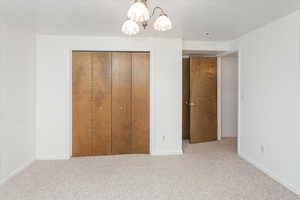 Unfurnished bedroom featuring light carpet, a notable chandelier, and a closet