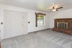 Unfurnished living room featuring a brick fireplace, a textured ceiling, carpet, and ceiling fan