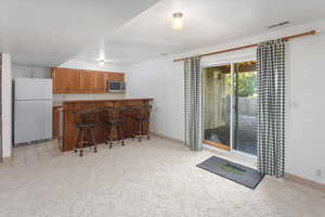 Kitchen featuring light colored carpet, stainless steel microwave, a breakfast bar, and white fridge