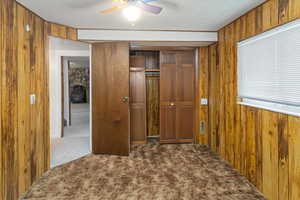 Unfurnished bedroom with a closet, carpet flooring, wood walls, a fireplace, and ceiling fan