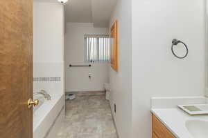 Bathroom featuring tiled bath, vanity, and toilet