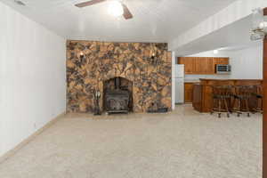 Carpeted living room featuring indoor bar, ceiling fan, and a wood stove