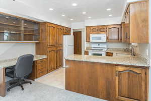 Kitchen with kitchen peninsula, sink, white appliances, built in desk, and light stone countertops