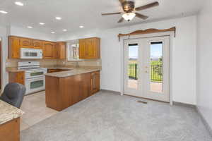 Kitchen featuring light carpet, white appliances, a textured ceiling, and a healthy amount of sunlight