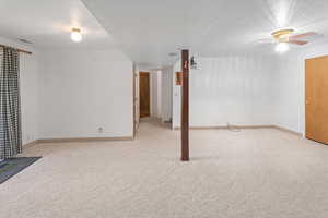 Basement featuring a textured ceiling, ceiling fan, and light carpet