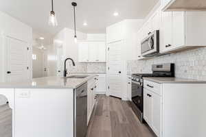 Kitchen with appliances with stainless steel finishes, pendant lighting, sink, white cabinetry, and a kitchen island with sink