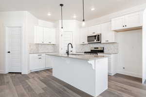 Kitchen with stainless steel appliances, an island with sink, pendant lighting, sink, and white cabinetry