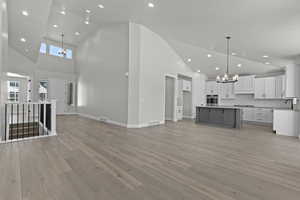 Kitchen with white cabinets, hanging light fixtures, a kitchen island, high vaulted ceiling, and stainless steel oven