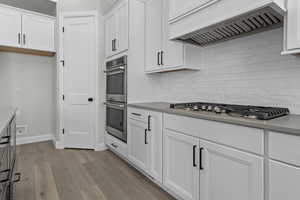 Kitchen with custom range hood, backsplash, stainless steel appliances, and white cabinets