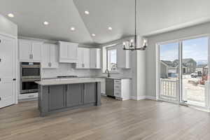 Kitchen with a healthy amount of sunlight, lofted ceiling, white cabinetry, and stainless steel appliances