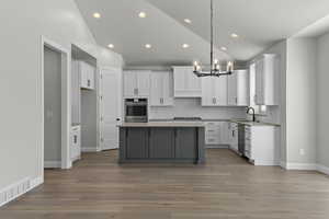 Kitchen featuring appliances with stainless steel finishes, light hardwood / wood-style floors, white cabinetry, pendant lighting, and a center island