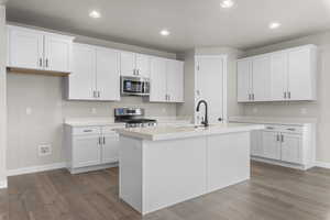 Kitchen featuring hardwood / wood-style flooring, white cabinetry, an island with sink, and appliances with stainless steel finishes