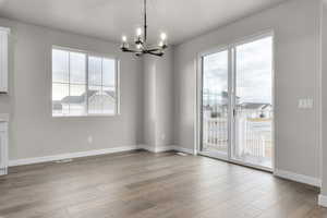 Unfurnished dining area featuring light hardwood / wood-style floors, an inviting chandelier, and a healthy amount of sunlight